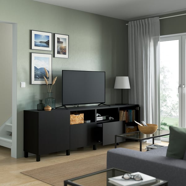 Green living room, black tv stand with flat screen, photos, lamp, and glass coffee table with wooden bowl.