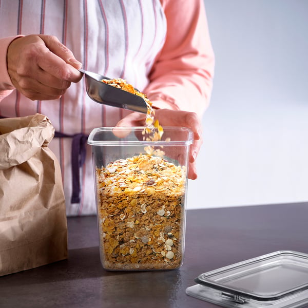 Person pours cereal from paper bag into clear jar with airtight lid on kitchen counter.