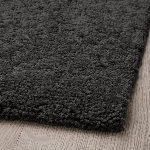 Dark grey, soft rug with textured yarn, laid on wooden floor.