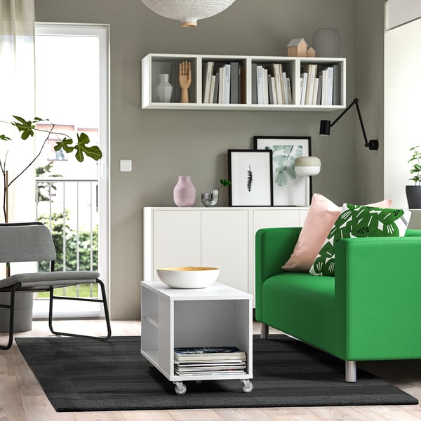 Modern living room with grey rug, green sofa, and white table.