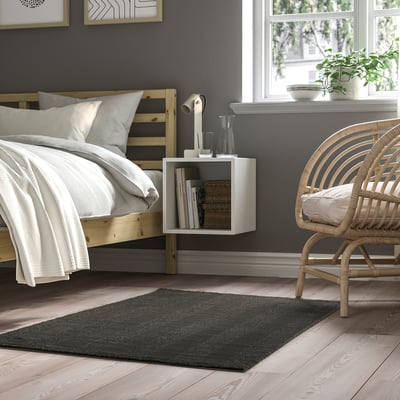 Grey striped rug near wooden bed, chair, and shelf with lamp.
