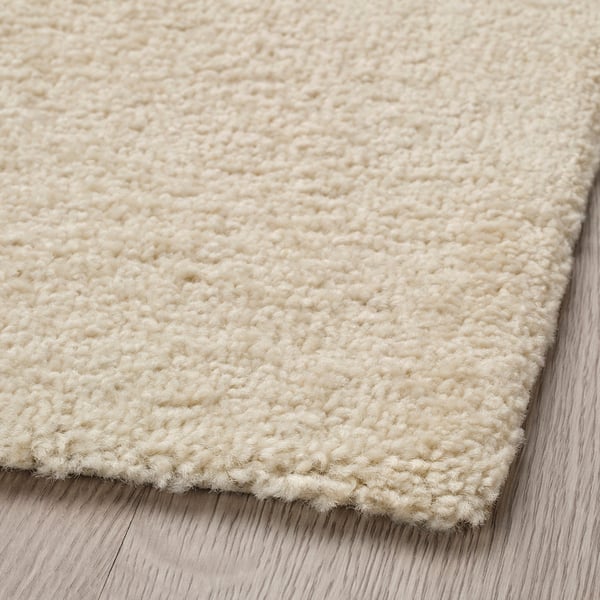 Close-up of soft, off-white, low-pile rug on wooden floor. High-quality texture, curly yarn detail.