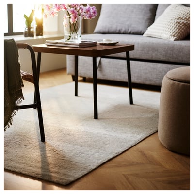 Living room with grey sofa, coffee table, white rug, pink flowers, and brown ottoman.