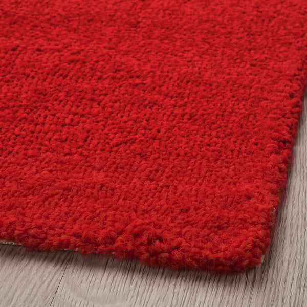 Bright red textured rug on wooden floor, soft, warm.