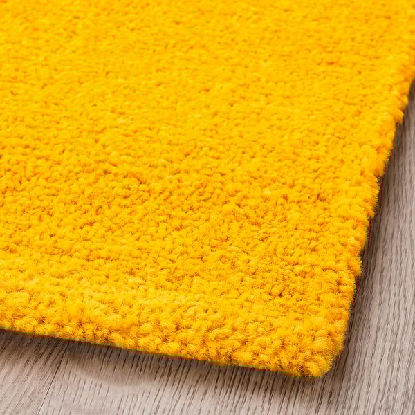 Bright yellow textured rug with curly yarns, soft and inviting texture, laid on wooden floor.