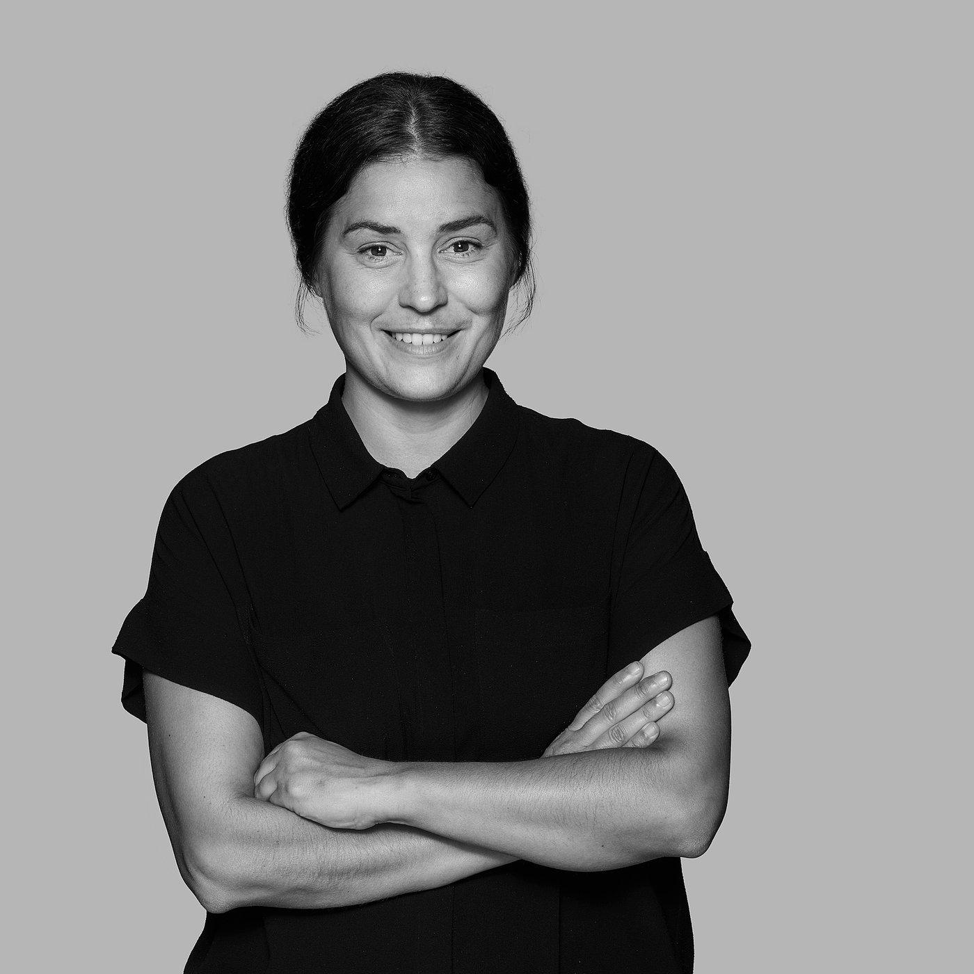 Black and white portrait of the smiling desinger with arms crossed, wearing a dark top.