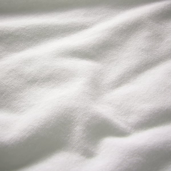 Close-up of smooth, high-quality white fabric, likely 100% cotton. Shows soft texture and slight folds.
