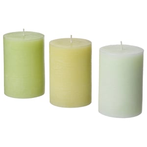 Three cylindrical candles in shades of green, cream, and white, each with a wick at the top, arranged in a row.