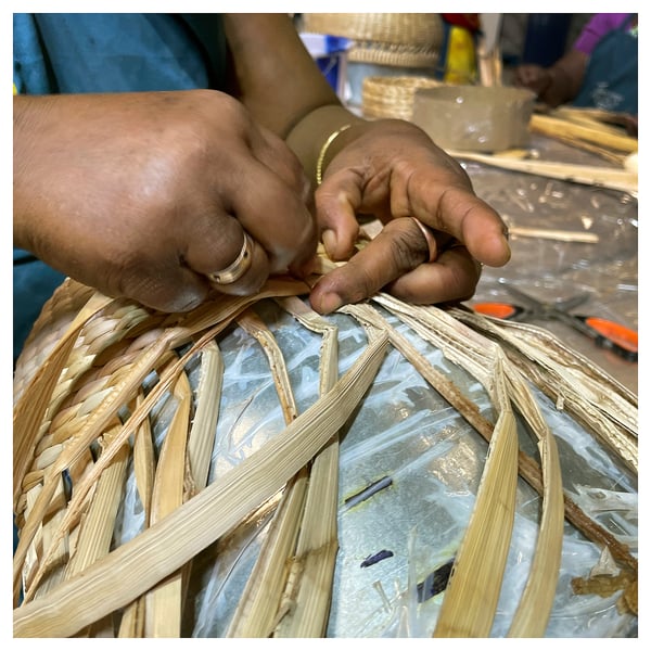 A person weaves a basket using natural fibres, showcasing manual craftsmanship.