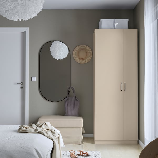 Minimalist bedroom with beige PAX wardrobe, white bed, fluffy light, round mirror, purple bag, straw hat.