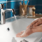 Händewaschen unter verchromtem Wasserhahn, blau gefliestes Badezimmer, modernes Design.