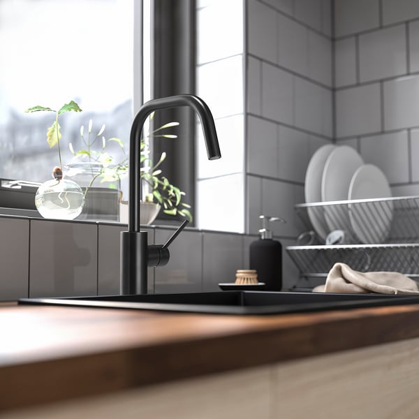 Moderne Küchenspüle mit schwarzer ÄLMAREN-Armatur, wasser- und energiesparend, hoher Auslauf für einfache Reinigung, Fensternähe mit Pflanzen und Geschirr.