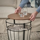 Die Person greift nach einem Glas auf dem ÄNGESBYN-Tisch und demonstriert die Verwendung als Café- oder Beistelltisch mit Stauraum.