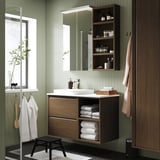 Grünes Badezimmer mit dunklem Holzwaschtisch, weißem Waschbecken, Spiegel und Stauraum.