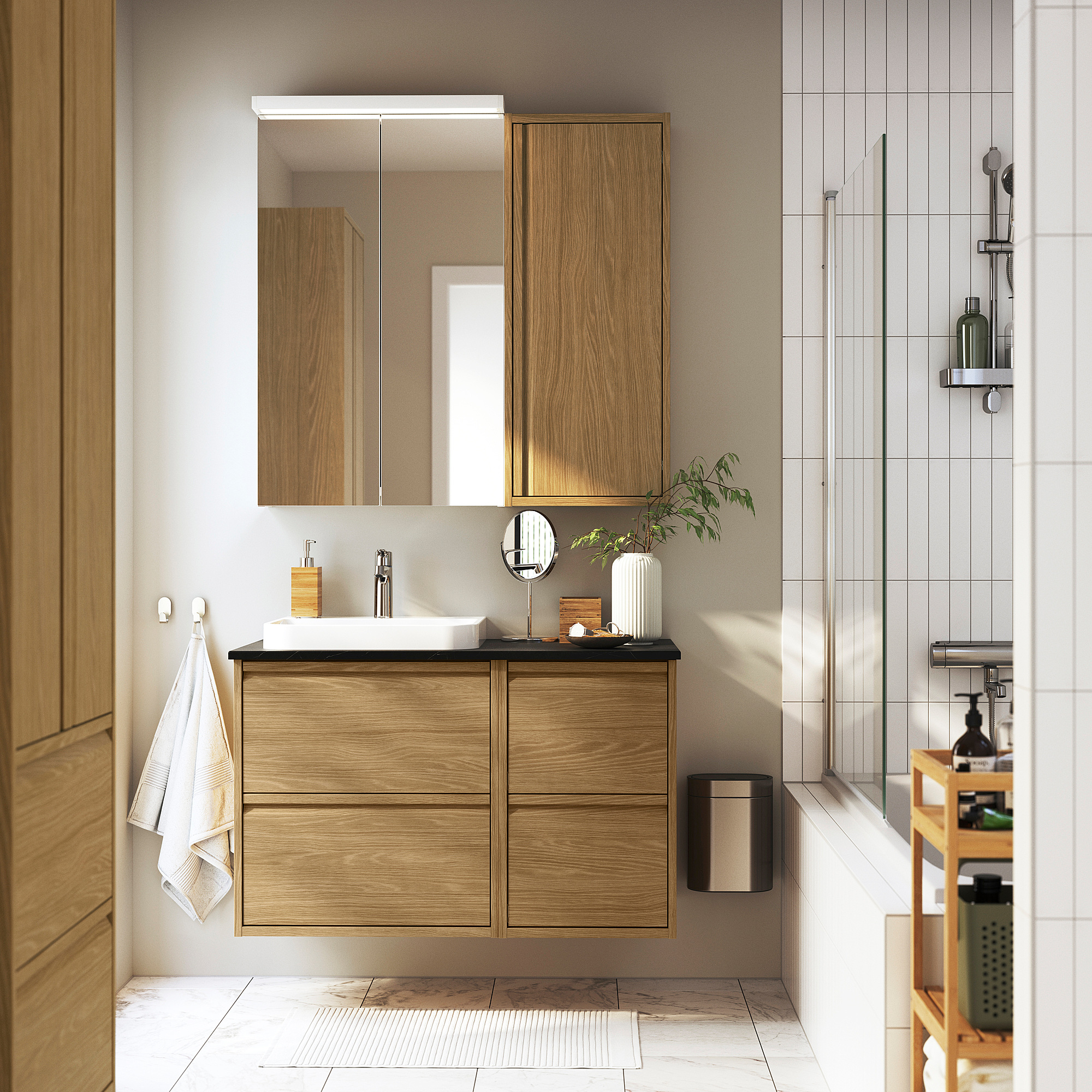 Modernes Badezimmer mit ÄNGSJÖN-Kollektion: schwimmender hellbrauner Waschtisch, Spiegel, Waschbecken, Glasdusche, Holzregal.