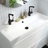 Modernes Waschbecken mit eleganter weißer Arbeitsplatte und schwarzen Wasserhähnen, einschließlich Seifenschale und Spender.