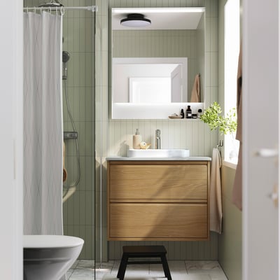 Modernes Badezimmer mit hellgrünen Fliesen, Holzschrank, weißem Waschbecken und Spiegel.