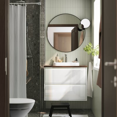 Modernes Badezimmer mit glänzendem ÄNGSJÖN-Waschtisch, halbvertieftem Waschbecken, dunklem Vorhang, Spiegel und kleiner Pflanze.