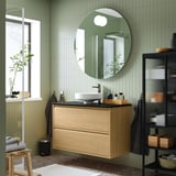 Modernes Badezimmer mit Holzwaschtisch, Spiegel, grünen Fliesen und glänzend schwarzer Theke.