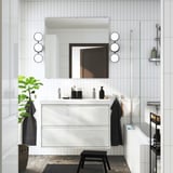 Modernes weißes Badezimmer mit ÄNGSJÖN-Waschbeckenschrank, Doppelbecken, schwarzen Akzenten und runden Leuchten.