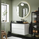 Modernes ÄNGSJÖN-Badezimmer: weißer Schrank, runder Spiegel, dunkles Waschbecken; Wandmontage mit grün gefliesten Wänden und schwarzen Armaturen.