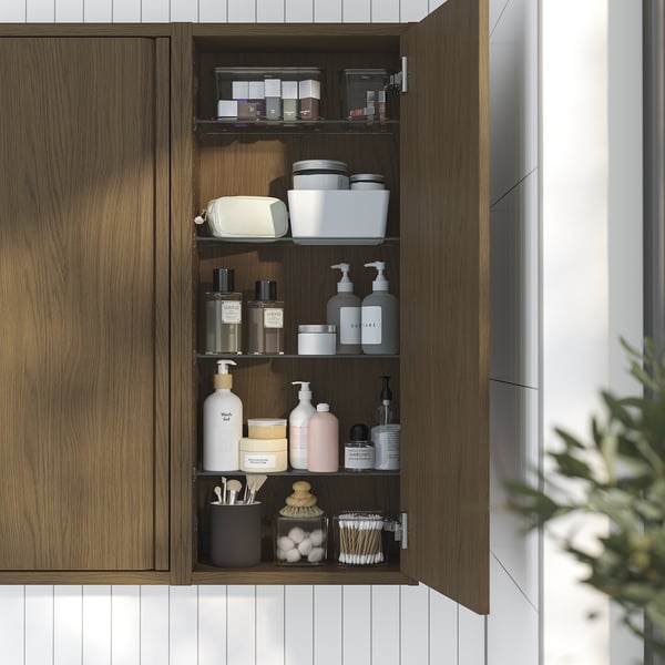Wandmontierter Badezimmerschrank aus Holz, offen mit Toilettenartikeln, dunklen Griffen, minimalistischer Stil.
