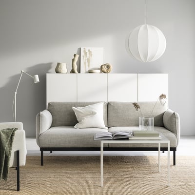 Modernes, minimalistisches Wohnzimmer mit grauem ÄPPLARYD-Sofa, weißen Akzenten und eleganten Möbeln.