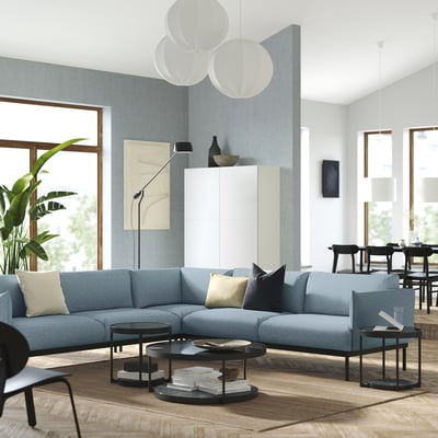 Modernes Wohnzimmer mit blauem ÄPPLARYD-Sofa, rundem Couchtisch, großen Fenstern und Hängelampen.