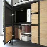 Offener Küchenschrank mit ÄSPINGE-Küchenzeile, Mikrowelle, Behältern und Schneidebrettern.