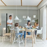 Die Familie genießt das Essen mit den Kindern, die auf bunten AGAM-Juniorstühlen sitzen, die für die Höhe eines Esstisches ausgelegt sind, in einer gemütlichen Küche.