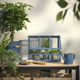 Blaues ÅKERBÄR Mini-Gewächshaus, klein, auf Holztisch mit Pflanzen, Gießkanne.