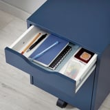 Blauer ALEX-Schubladenschrank mit Notizbüchern, Stiften und kleinen Aufbewahrungsgegenständen im Inneren, ideal für die Organisation auf dem Schreibtisch.