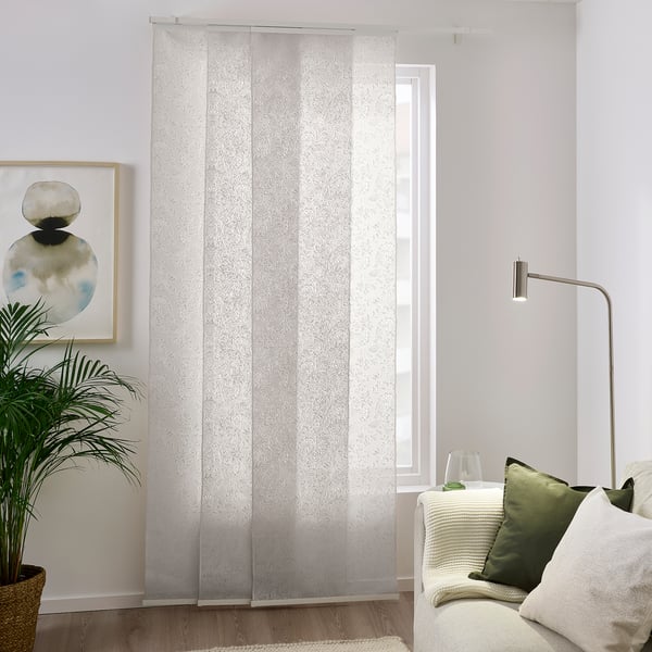 Weiße Vorhänge mit Blattmuster sorgen für ein helles, ruhiges Ambiente. Hergestellt aus recyceltem Polyester, bodenlang. Das Zimmer verfügt über eine Couch, Kissen und eine hohe Pflanze.