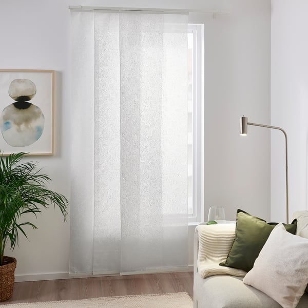 Weiße AMPELSÄV-Vorhänge mit Blattmuster hängen in der Nähe von Fenster und Couch und dämpfen das Licht. Pflanzen und Wandkunst sorgen für beruhigende Grüntöne.