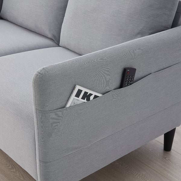 Modernes hellgraues Sofa mit Seitentaschen. In einer Tasche befindet sich ein Magazin, in der anderen eine Fernbedienung.