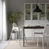 Modernes Esszimmer mit ANTILOP-Hochstuhl, weißem Tisch und Stühlen, Zimmerpflanze und Bücherregal.