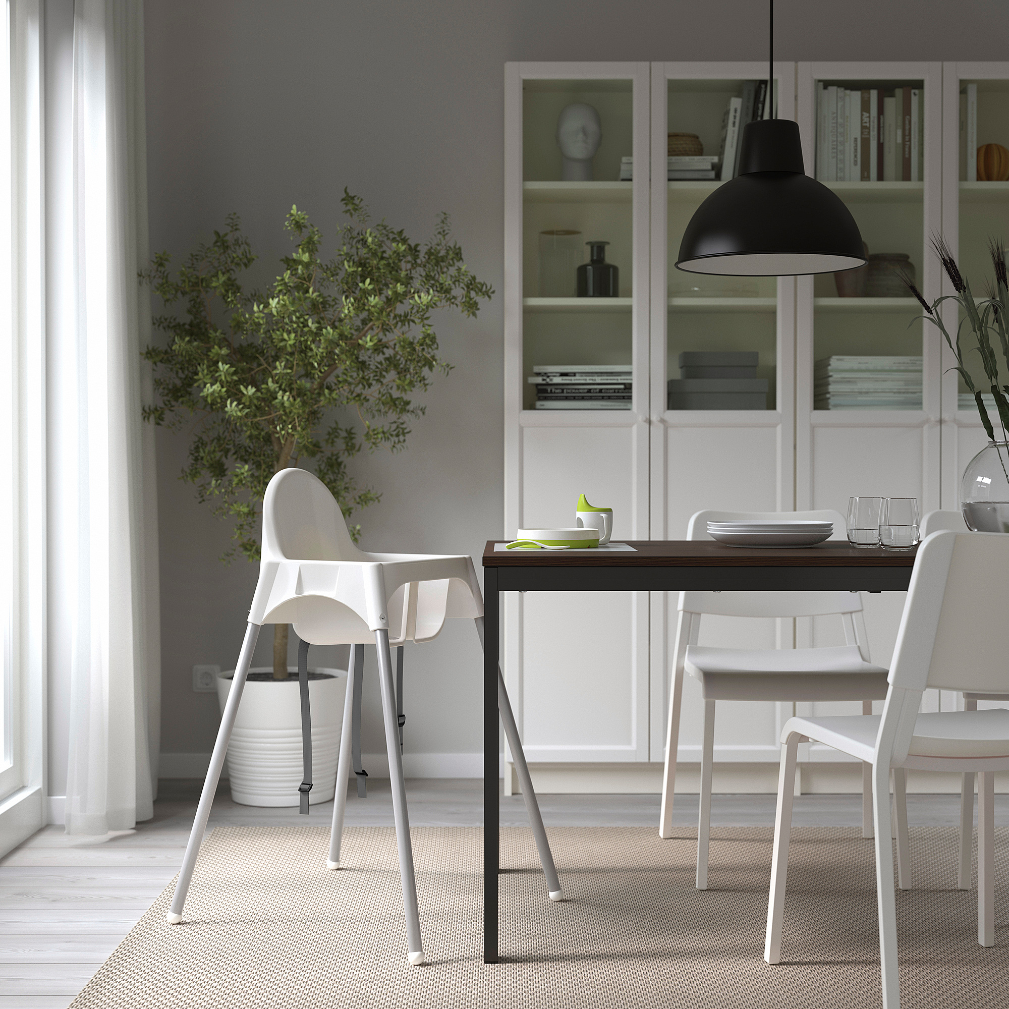 Modernes Esszimmer mit ANTILOP-Hochstuhl, weißem Tisch und Stühlen, Zimmerpflanze und Bücherregal.