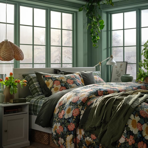 Dunkelblaue, florale ARENBOK-Bettdecke auf dem Bett mit grün karierten Kissen, hohen Fenstern.