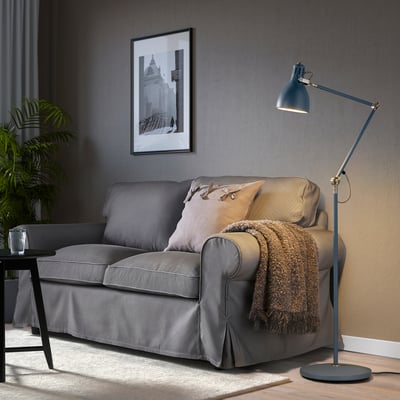 Graue ARÖD Stehleuchte neben einem grauen Sofa, hoch und verstellbar, sticht hervor.