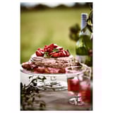 Erdbeerkuchen auf Klarglasständer mit Weinglas und Flasche, Außeneinstellung.