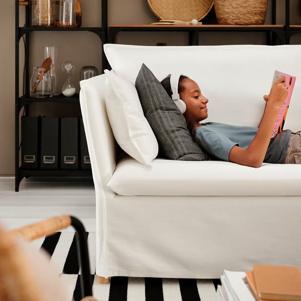 Die Person entspannt sich auf dem Sofa, liest, im gemütlichen Wohnzimmer mit Teppich und Regalen.