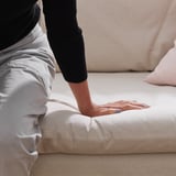Die Person testet die Weichheit eines weißen Schaumstoffblocks. Der Block ist Teil eines bequemen, leicht zu reinigenden Sofas mit einem abnehmbaren, maschinenwaschbaren Bezug.