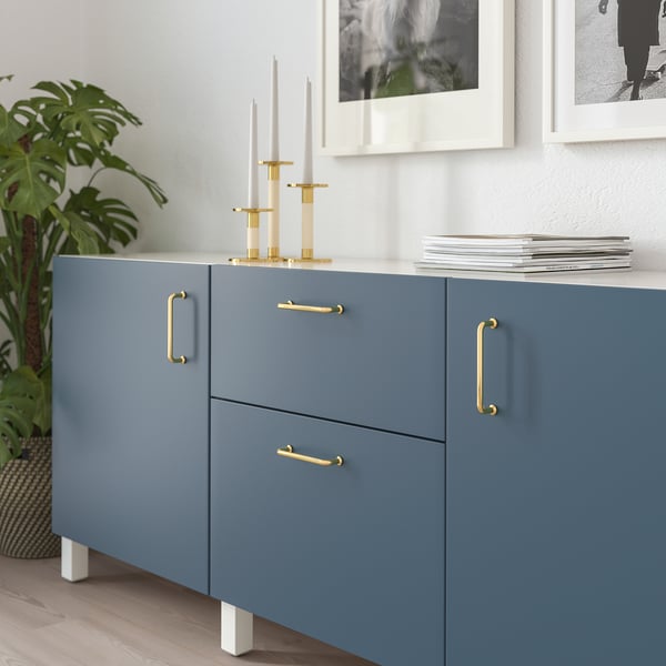 Blauer Schrank mit goldenen Griffen, verziert mit Kerzenständern und Zeitschriften; Geeignet für ein modernes Zuhause.