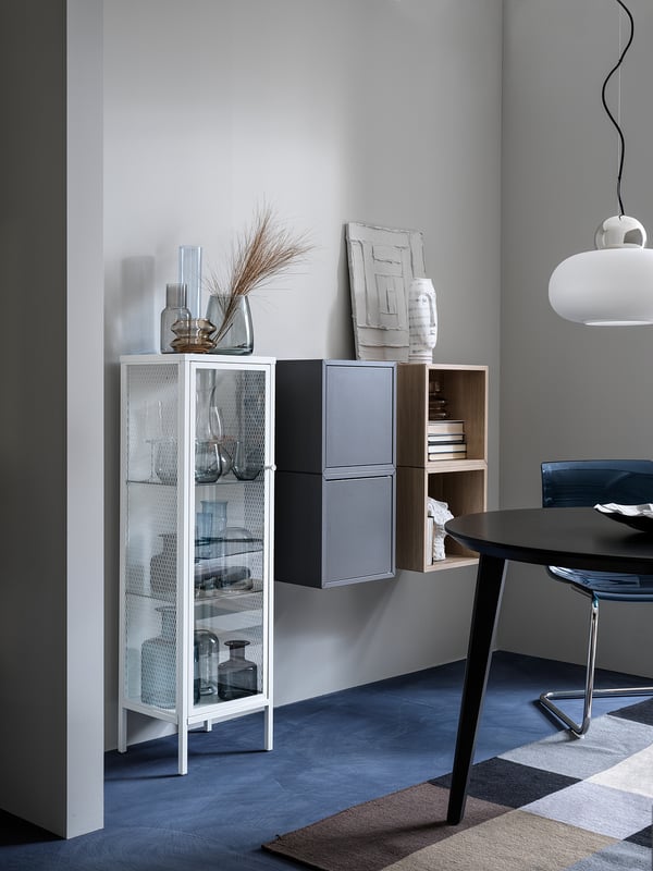Modernes Wohnzimmer mit weißem Schrank, Glasgegenständen, Vasen, Kunst, schwarzem Tisch und Pendelleuchte.