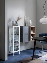 Modernes Wohnzimmer mit weißem Schrank, Glasgegenständen, Vasen, Kunst, schwarzem Tisch und Pendelleuchte.