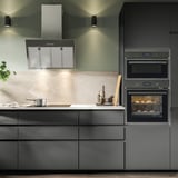 Moderne Küche mit schwarzen Schränken, Dunstabzugshaube aus Edelstahl, eingebautem Backofen und Arbeitsplatten.