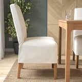 Moderne Esseinrichtung mit beigem Polsterstuhl, Holztisch und Glasbecher.
