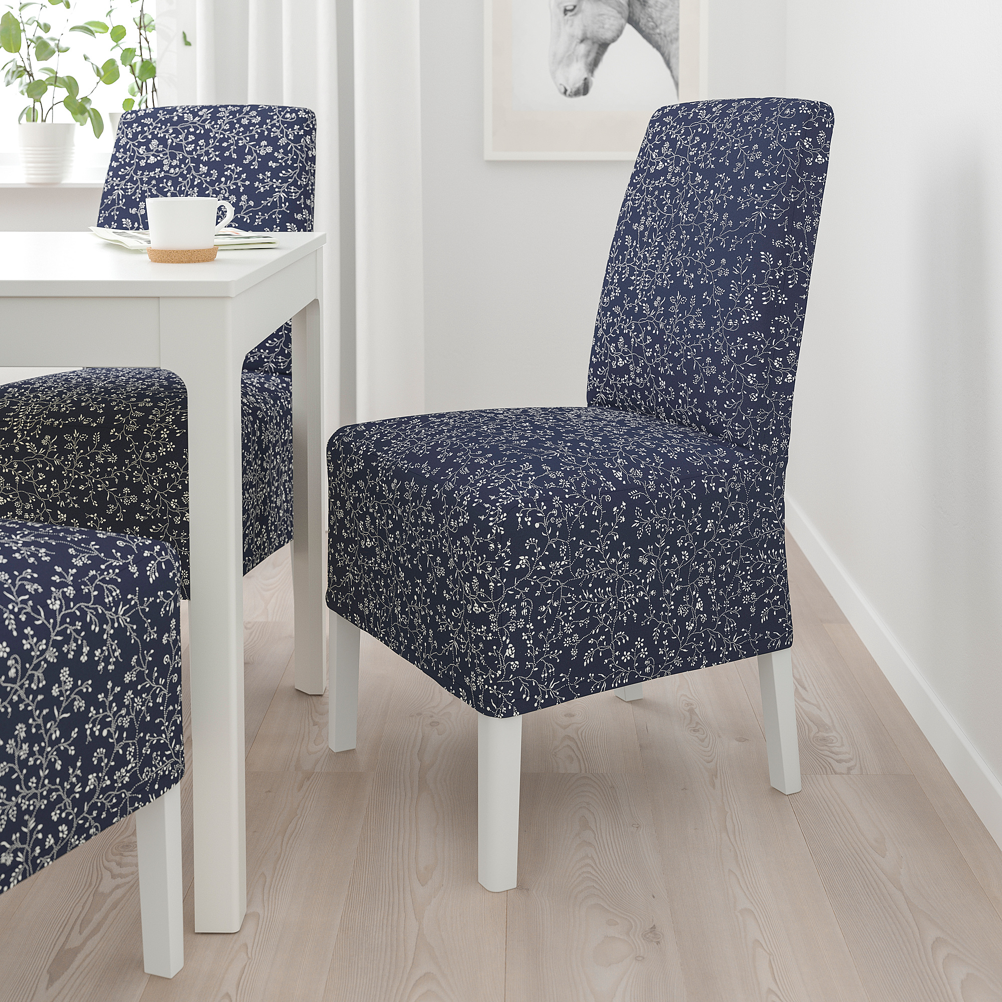 Zwei marineblaue geblümte BERGMUND Stühle mit weißem Esstisch. Hohe Rückenlehne, etwas höher als der Tisch. Holzböden, weiße Kaffeetasse auf dem Tisch.