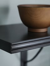 Ein schwarzes Regal von BERGSHULT mit einer Holzschale. Das Regal hat eine glatte Kante und ist aus Spanplatten gefertigt.