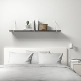 Minimalistisches weißes Schlafzimmer mit BERGSHULT-Wandregal mit Büchern, Pflanzen und Korb über einem ordentlich gemachten Bett mit weißer Bettwäsche.